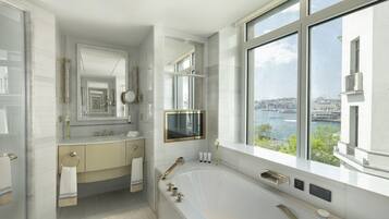 Ein modernes Badezimmer mit einer großen Badewanne, einem Waschtisch mit Spiegel und Blick auf eine Stadtkulisse durch große Fenster.