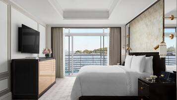A hotel room with a large bed, a TV, a desk with a lamp, and a view of the water.