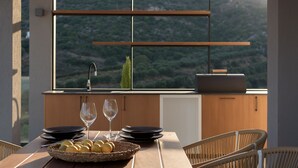 A dining area with a table set for two, a basket of lemons, and a view of a mountainous landscape through large windows. - Mayana Luxury Villa, an infinite blue experience (Rethymno)