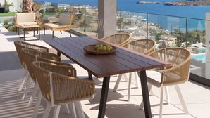 A terrace with a wooden table, wicker chairs, and a view of the sea and hills. - Mayana Luxury Villa, an infinite blue experience (Rethymno)