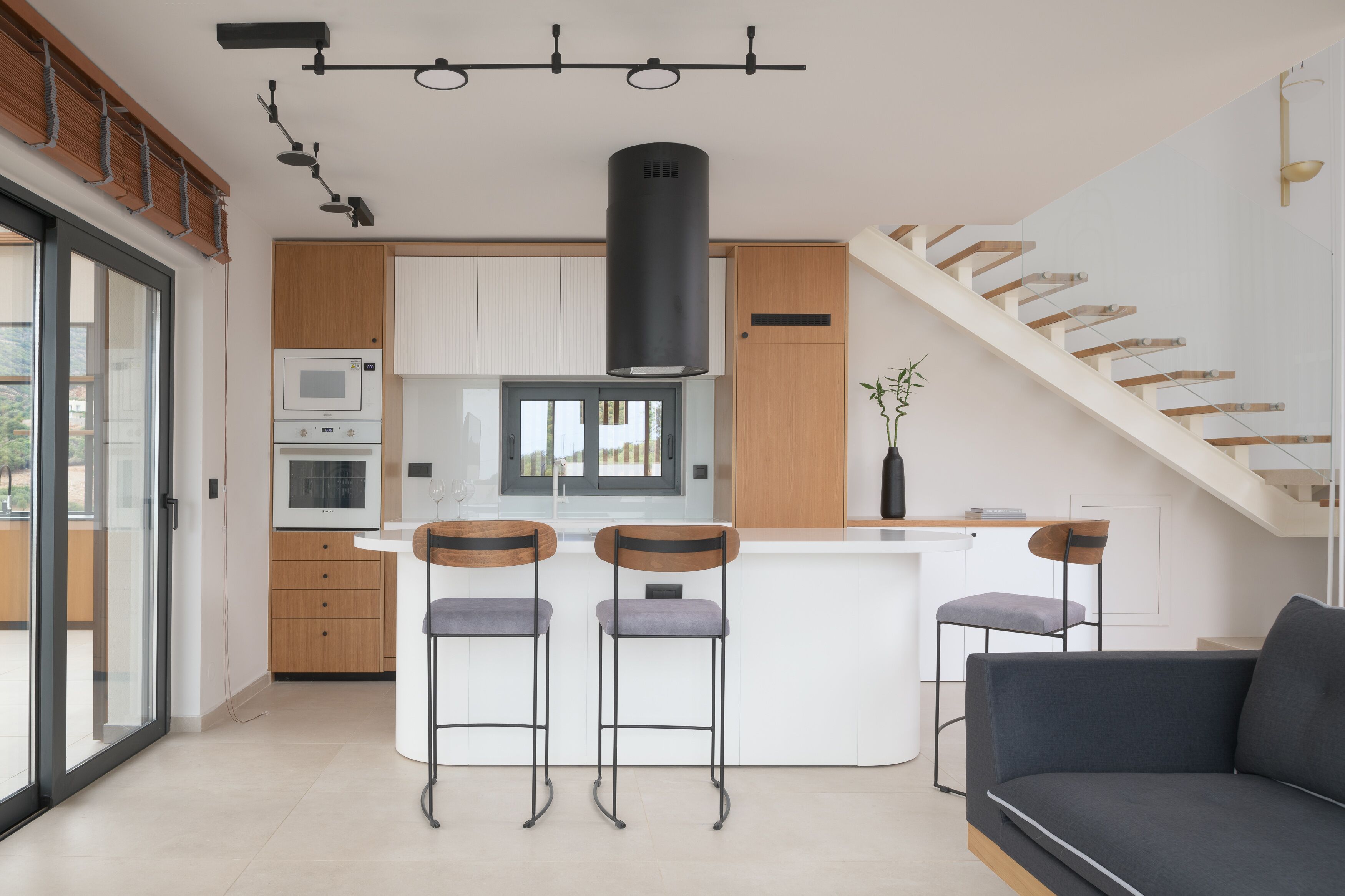 A modern kitchen with a central island, bar stools, a built-in oven, and a large black range hood.