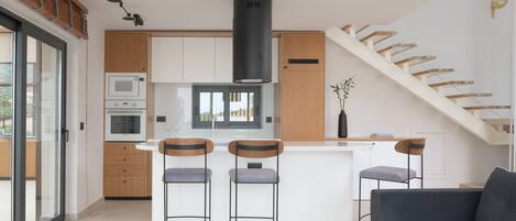 A modern kitchen with a central island, bar stools, a built-in oven, and a large black range hood.