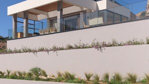 A modern two-story house with a flat roof, large glass windows, and a balcony with outdoor furniture. - Mayana Luxury Villa, an infinite blue experience (Rethymno)