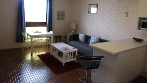 Een ruimtelijke leefruimte met een kitchenette, een eethoek en een zithoek met een bank en een stoel.