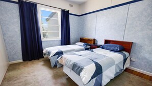 A bedroom with two beds, a window with curtains, and a wooden headboard. - Kalimna Holiday House: Relax and enjoy the magnificent 180-degree water views (Kalimna)