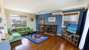 A living room with a green sofa, a coffee table, a fireplace, a TV, and a bookshelf. - Kalimna Holiday House: Relax and enjoy the magnificent 180-degree water views (Kalimna)