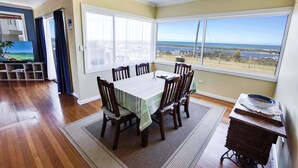 A dining area with a table and chairs, a view of the ocean, and a wooden floor. - Kalimna Holiday House: Relax and enjoy the magnificent 180-degree water views (Kalimna)