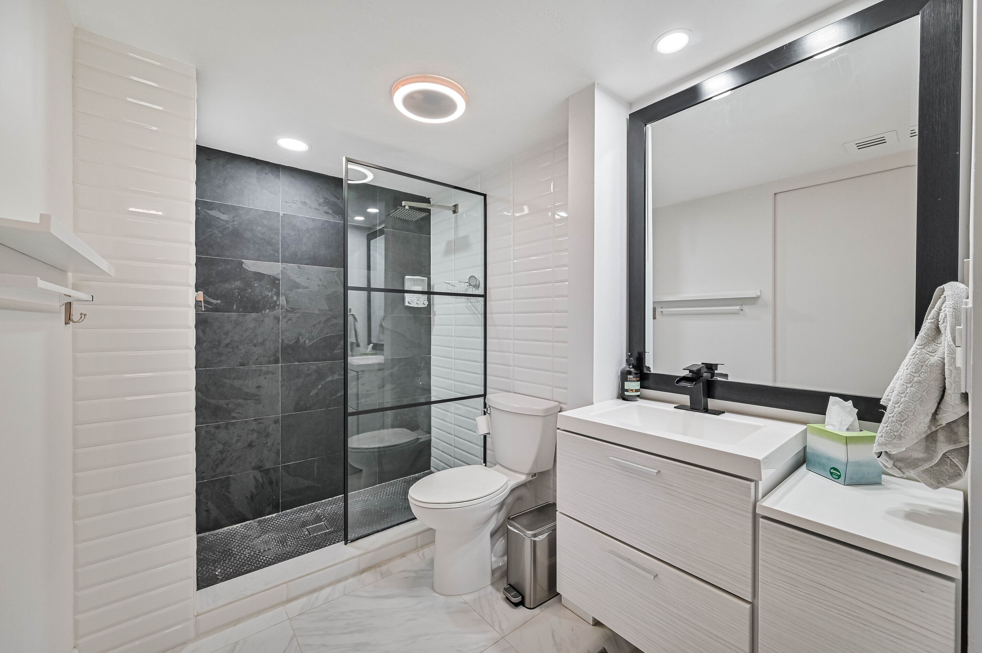 A modern bathroom with a glass-enclosed shower, a white toilet, and a vanity with a mirror.
