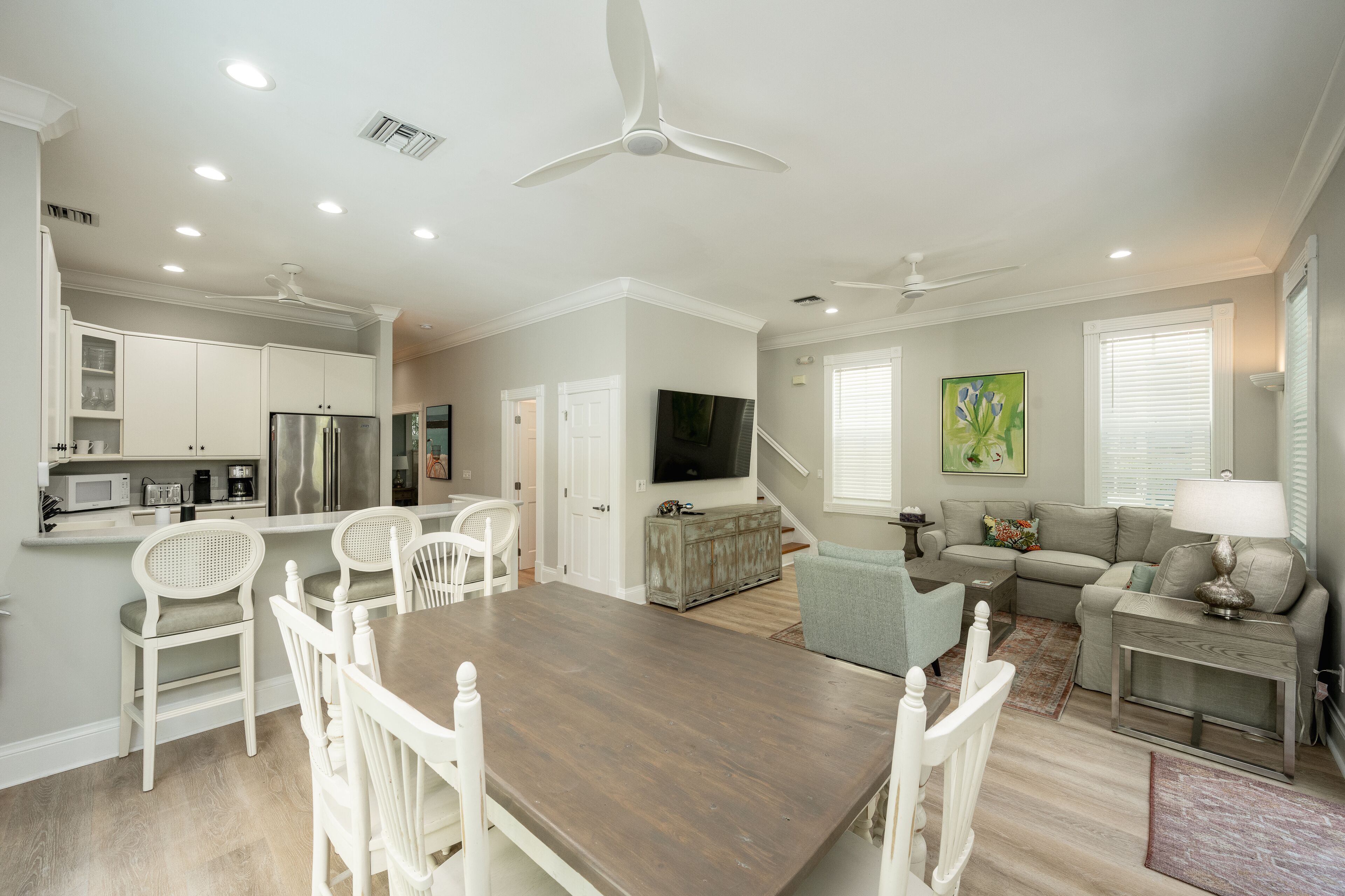 A spacious living area with a dining table, white chairs, a sofa, and a TV.