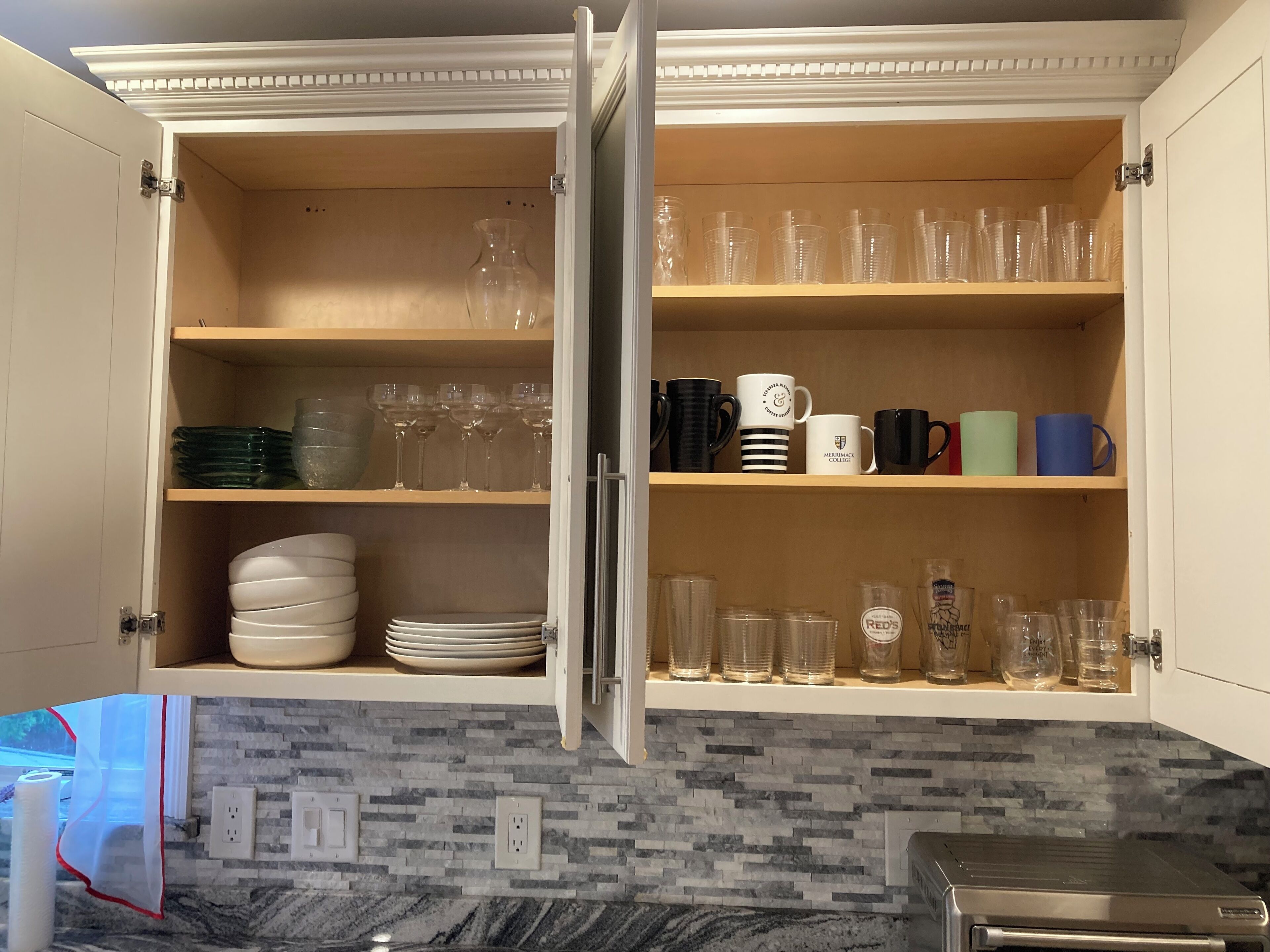 A kitchen with open cabinets displaying glassware, plates, and mugs.