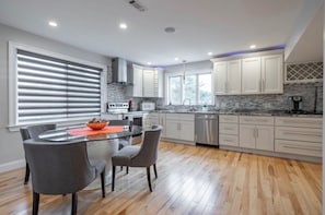 A modern kitchen with white cabinets, a granite countertop, and a dining area with a glass table and chairs.