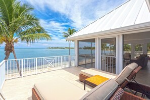 Ein überdachter Sitzbereich im Freien mit Blick auf den Ozean, ausgestattet mit Korbstühlen und einem Tisch, sowie eine nahegelegene Palme.