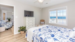Une chambre à coucher comprenant un lit, une commode, un téléviseur et une vue sur l’océan par la fenêtre.
