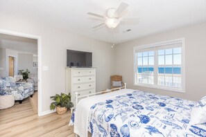 A bedroom with a bed, dresser, television, and a view of the ocean through a window.