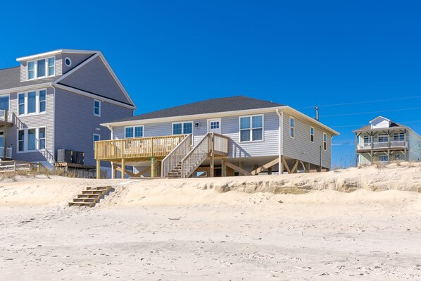 Una casa de playa de dos pisos con un muelle de madera y escaleras que suben al segundo piso.