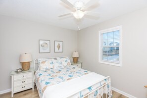 A bedroom with a bed, two bedside tables, a ceiling fan, and a window with blinds.