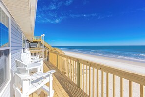 Una terraza de madera con sillas blancas, con vista a una playa y aguas azul cristalino.