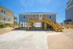 A two-story beach house with a wooden deck and a staircase leading to an upper level.