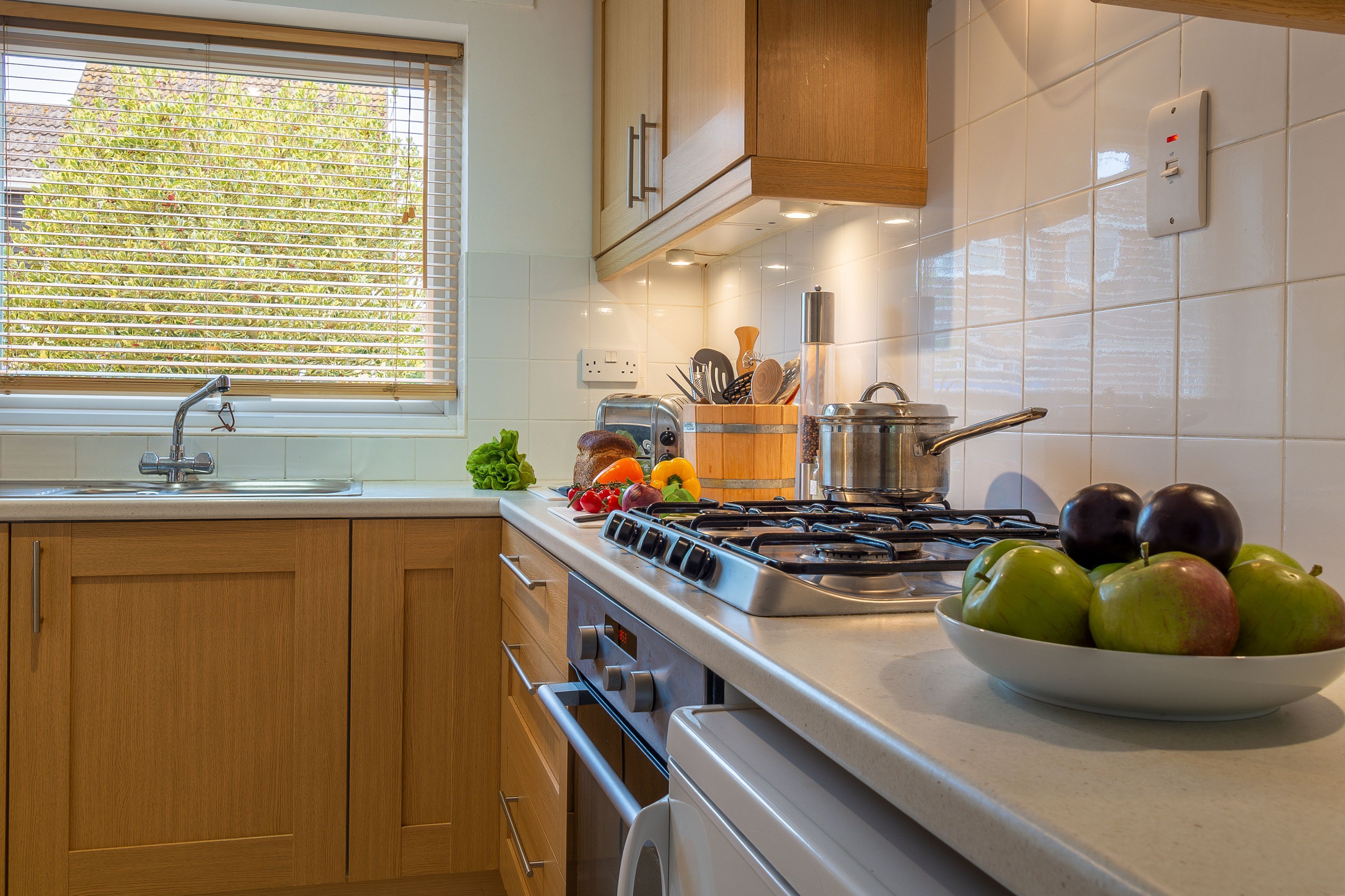 A modern kitchen with wooden cabinets, a stainless steel stove, and a bowl of apples on the counter.
