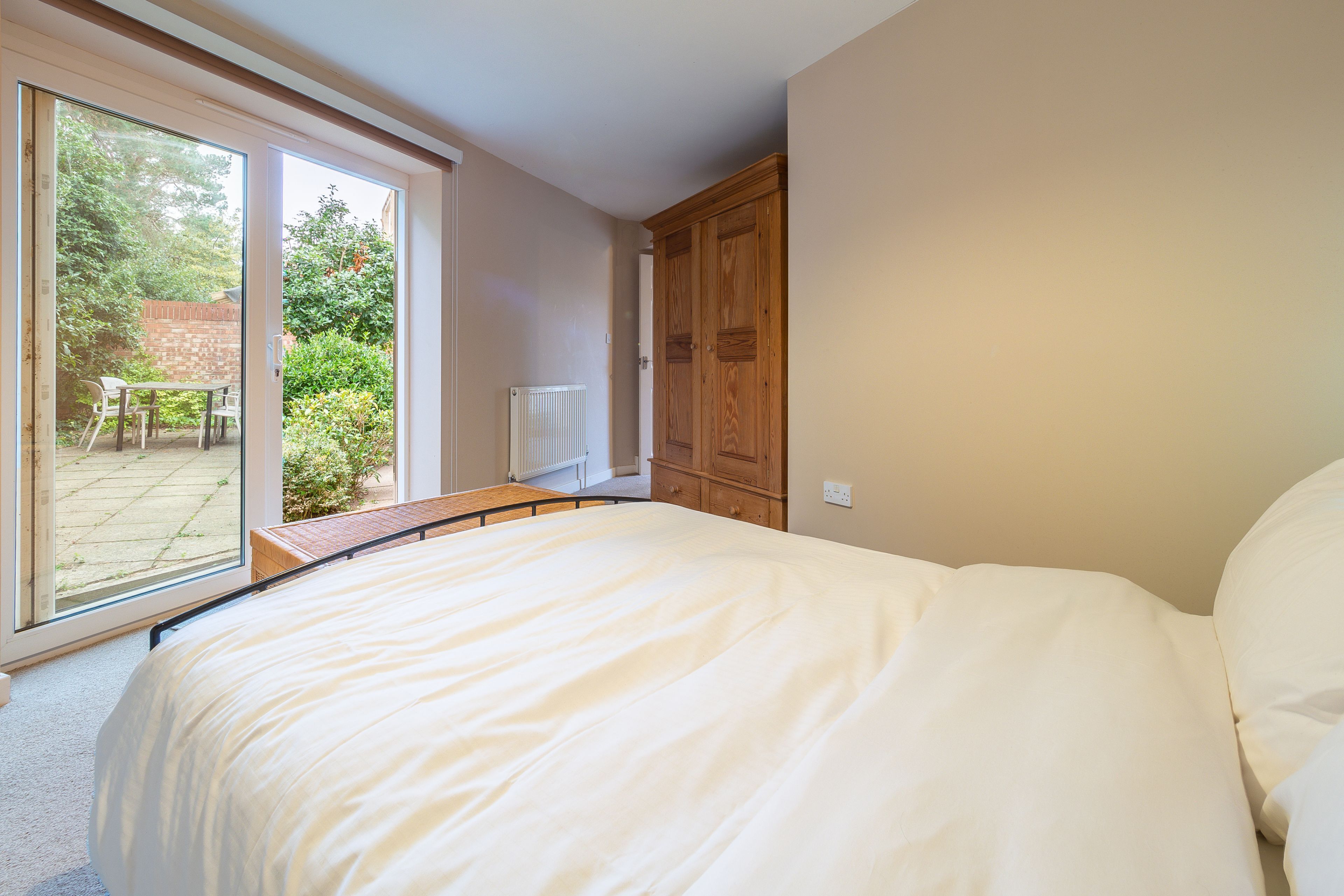 A bedroom with a large bed, a wooden wardrobe, and a sliding glass door leading to a patio with a table and chairs.