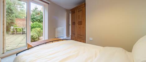 A bedroom with a large bed, a wooden wardrobe, and a sliding glass door leading to a patio with a table and chairs.