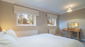 Un dormitorio con una cama grande, dos ventanas con persianas, un escritorio con silla y un espejo.