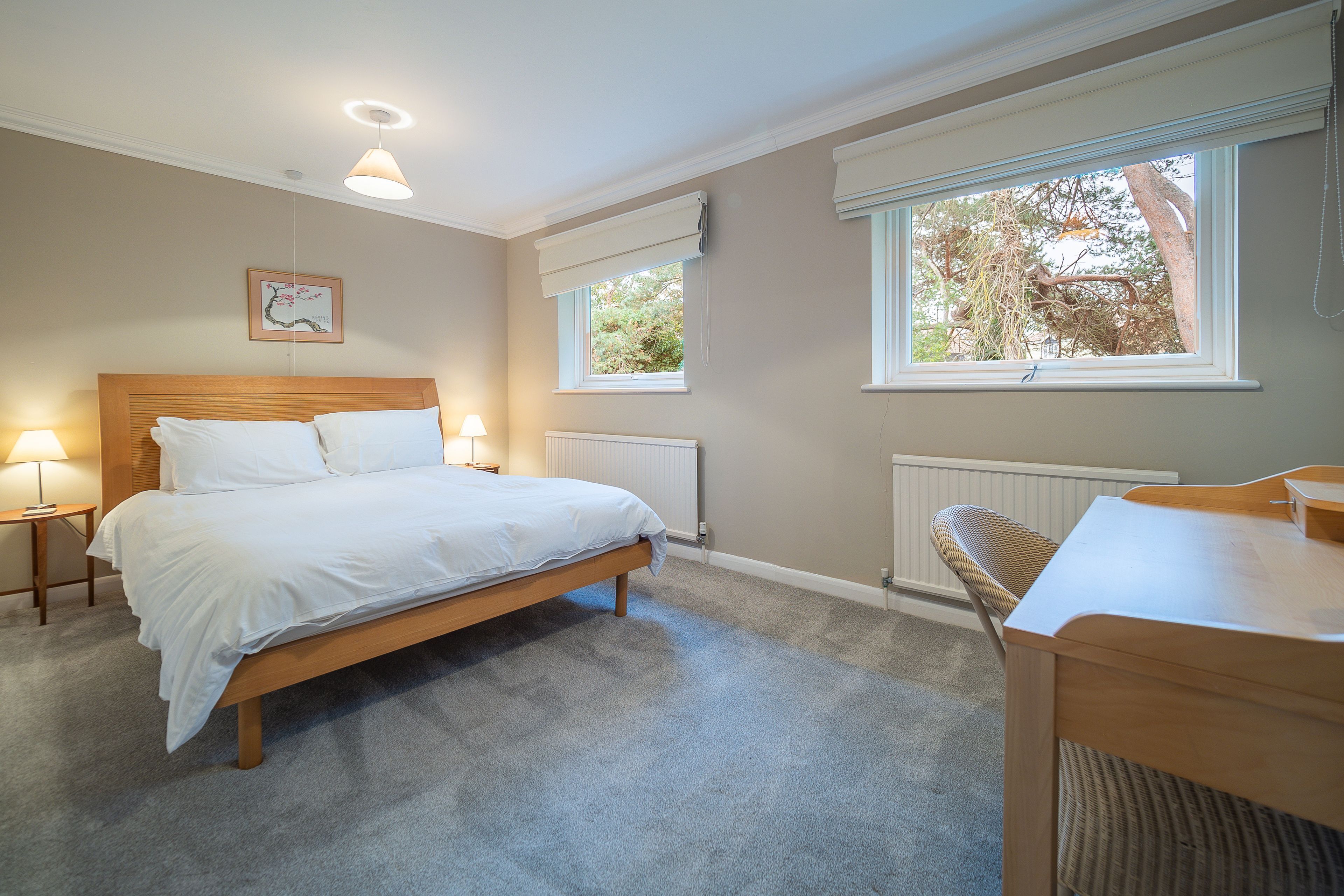 A bedroom with a wooden bed, two bedside lamps, a window with a view of trees, and a radiator.