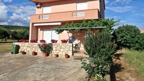 A two-story building with a stone facade, a red-tiled roof, and a balcony with potted plants.