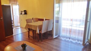 A dining area with a table and chairs, a clock on the wall, and a sliding glass door leading to an outdoor balcony.