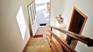 A staircase with wooden handrails and beige tiles, leading to an outdoor area with a tiled floor and a door.
