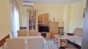 A living room with a sofa, TV, wooden cabinet, and a dining table with chairs.