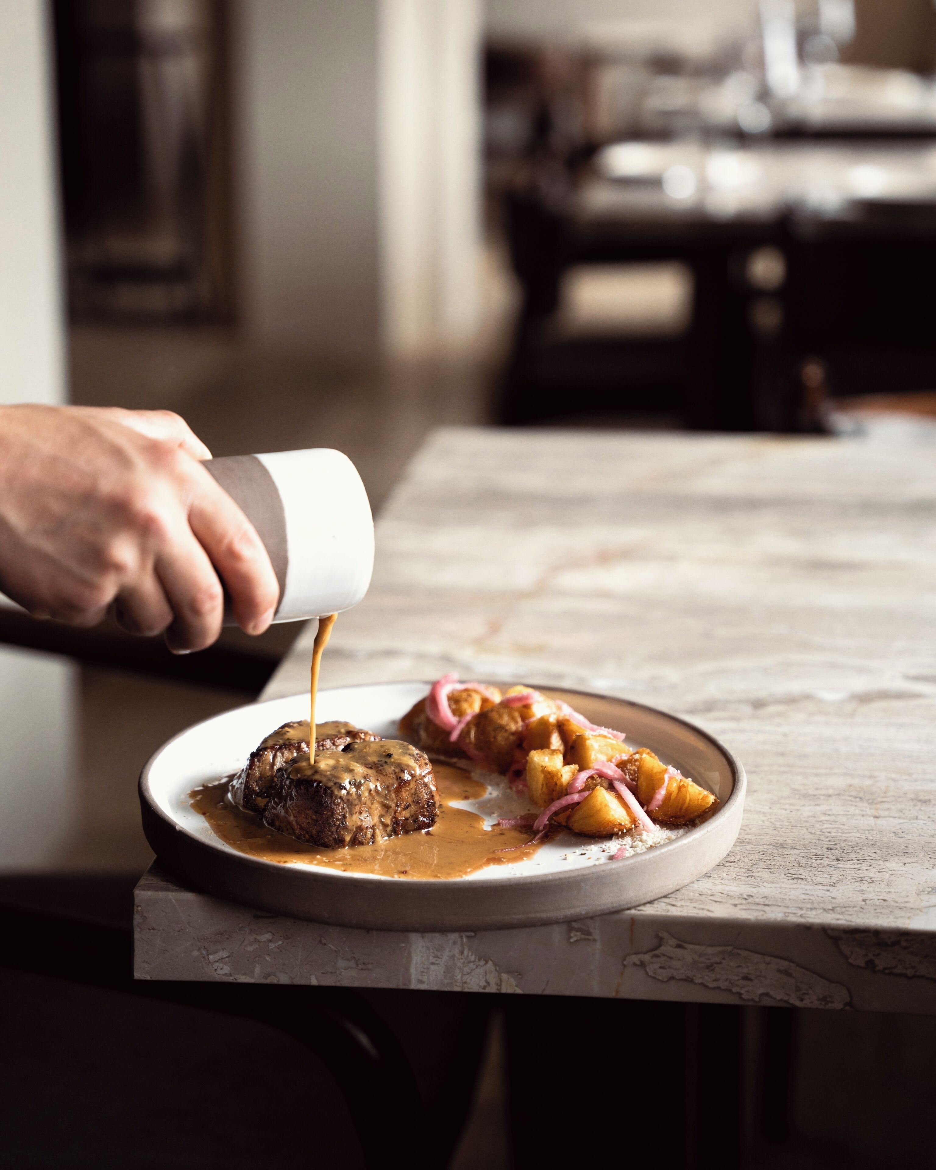 Un plato de comida con salsa, patatas y cebollas rojas sobre una mesa de mármol.