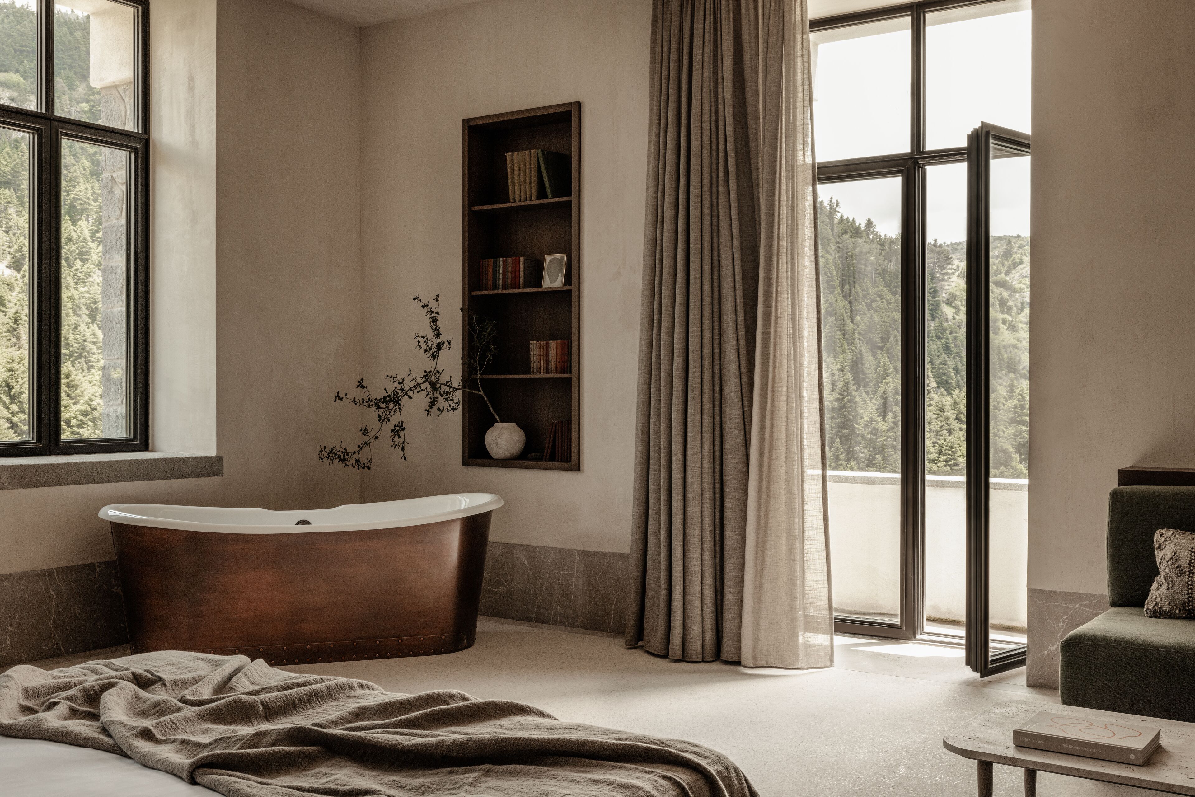 A modern bathroom with a freestanding bathtub, a bookshelf, and a view of a forest through large windows.