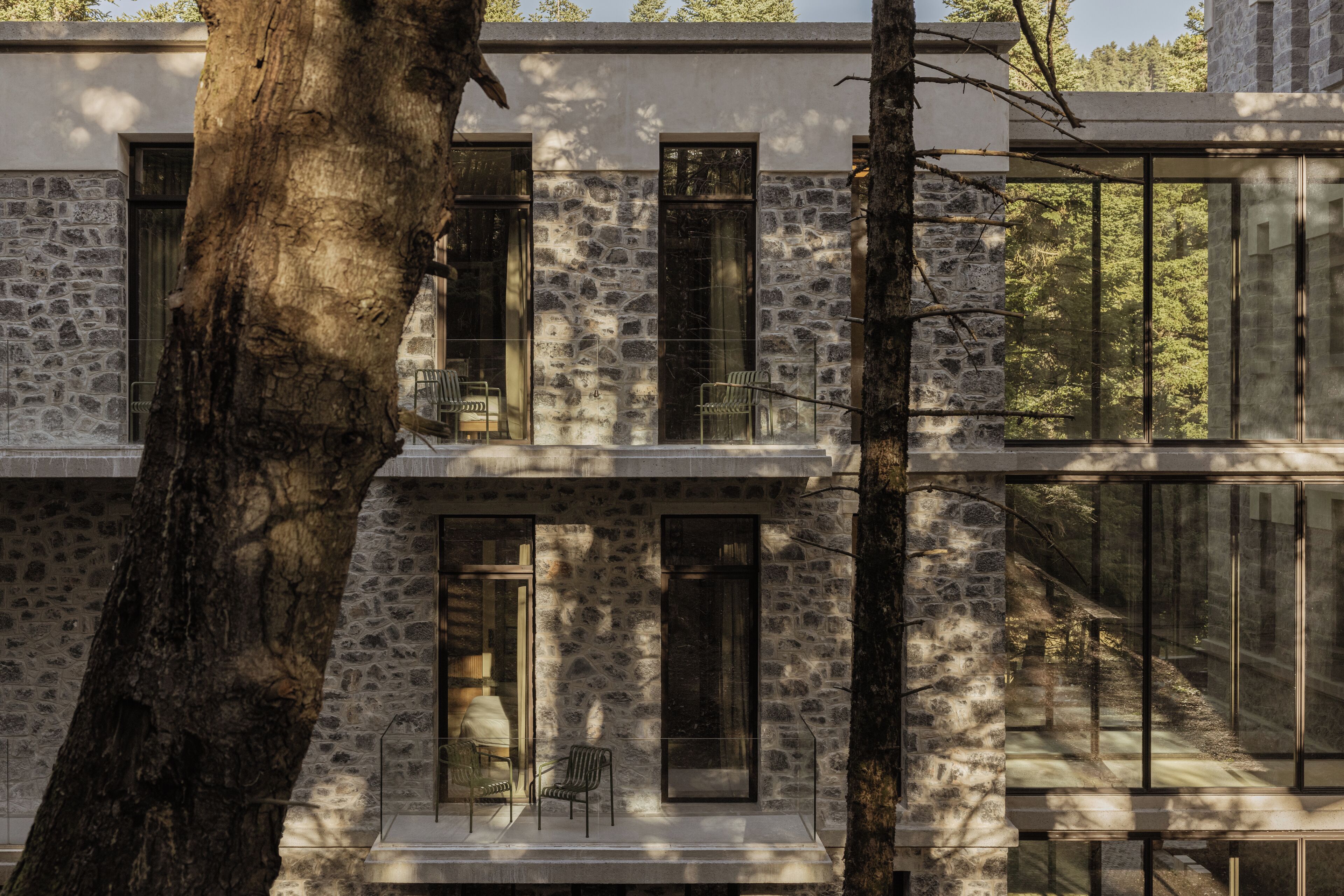 A modern building with stone facade and large windows, featuring a balcony with chairs.