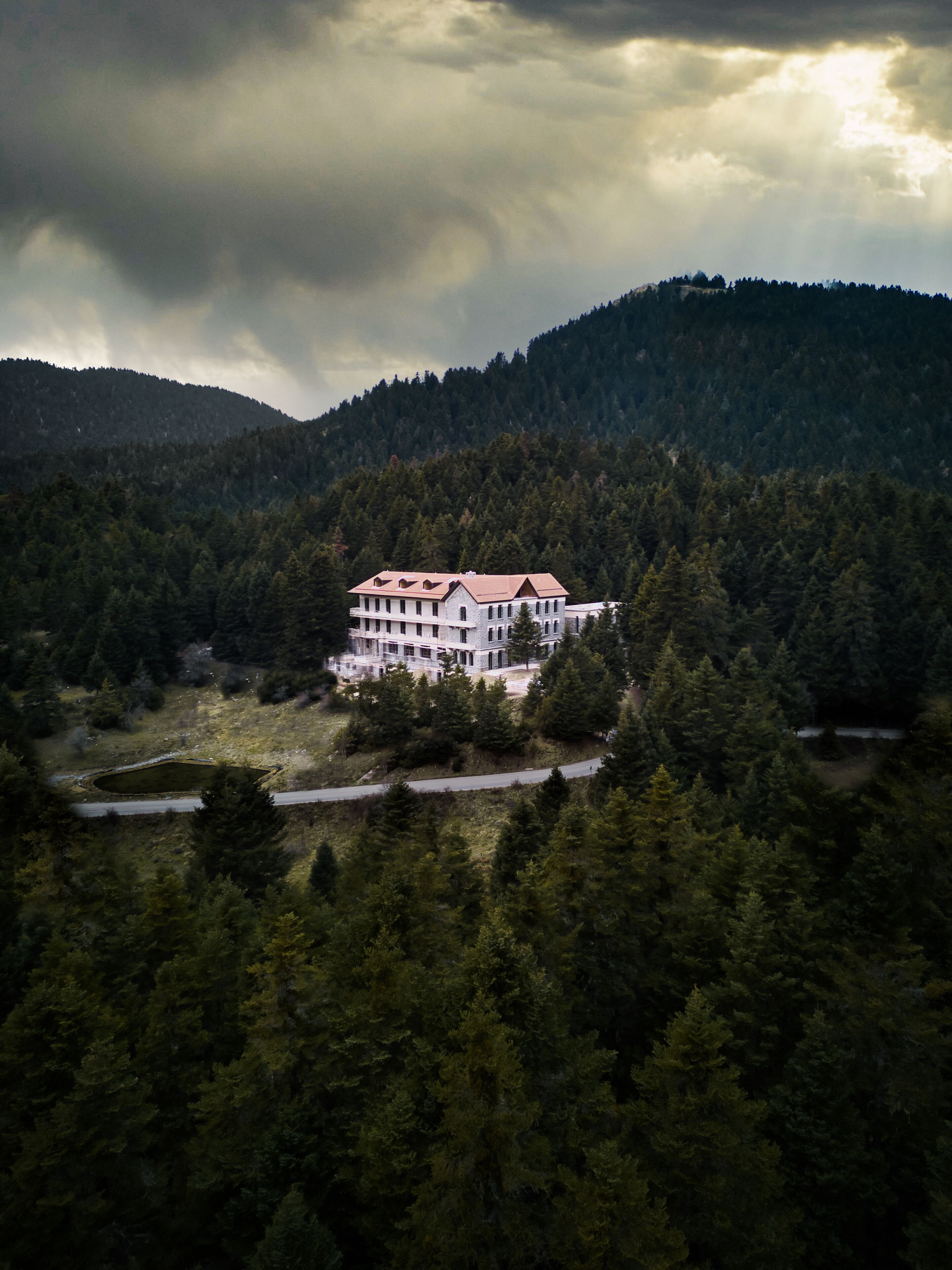A large, multi-story building surrounded by dense forest, with a road leading to it.