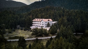 A large, multi-story building surrounded by dense forest, with a road leading to it.