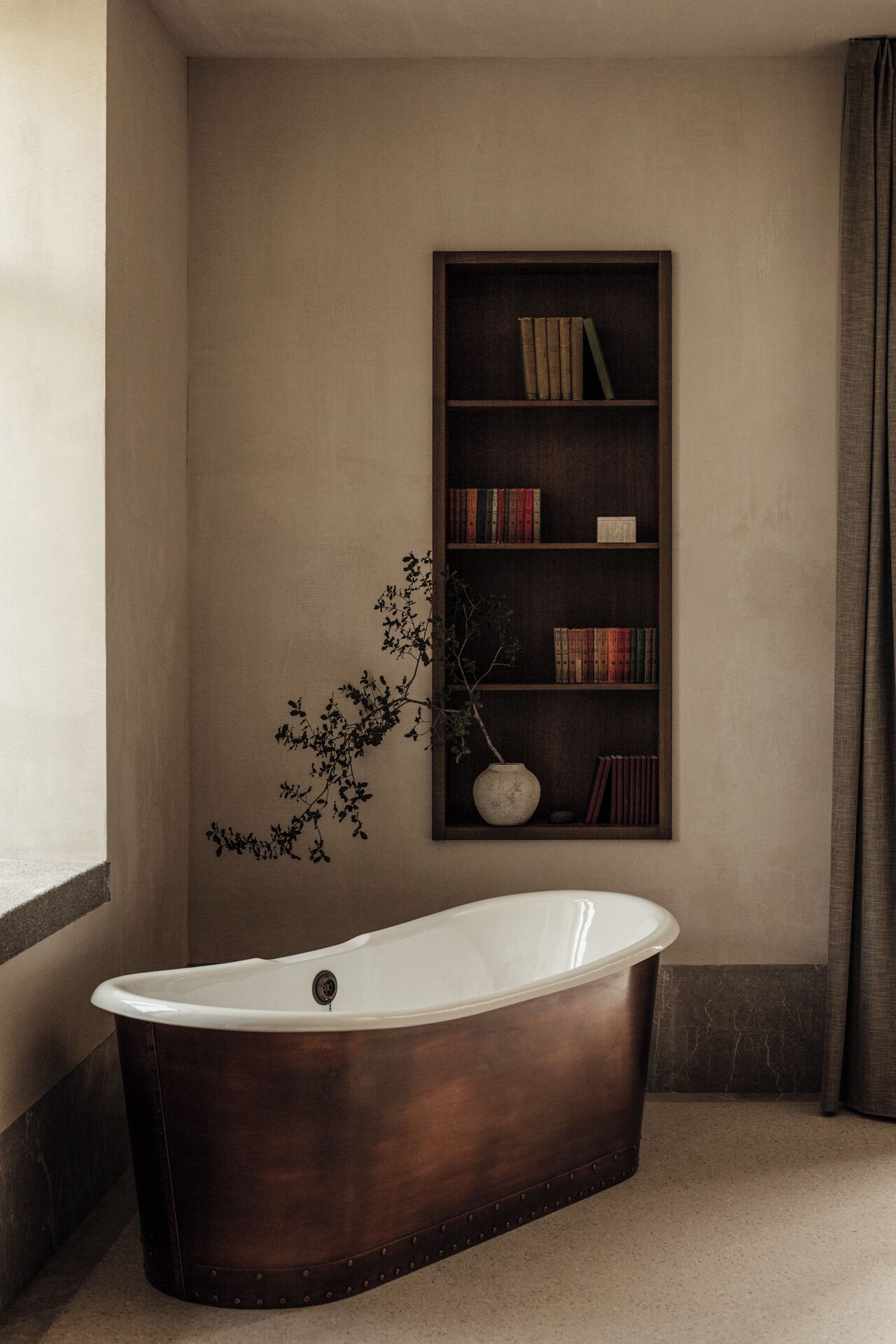 Une salle de bain avec une baignoire sur pieds, une bibliothèque remplie de livres et une plante en pot.