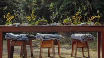 A wooden table with potted plants and a blanket on stools in an outdoor setting.