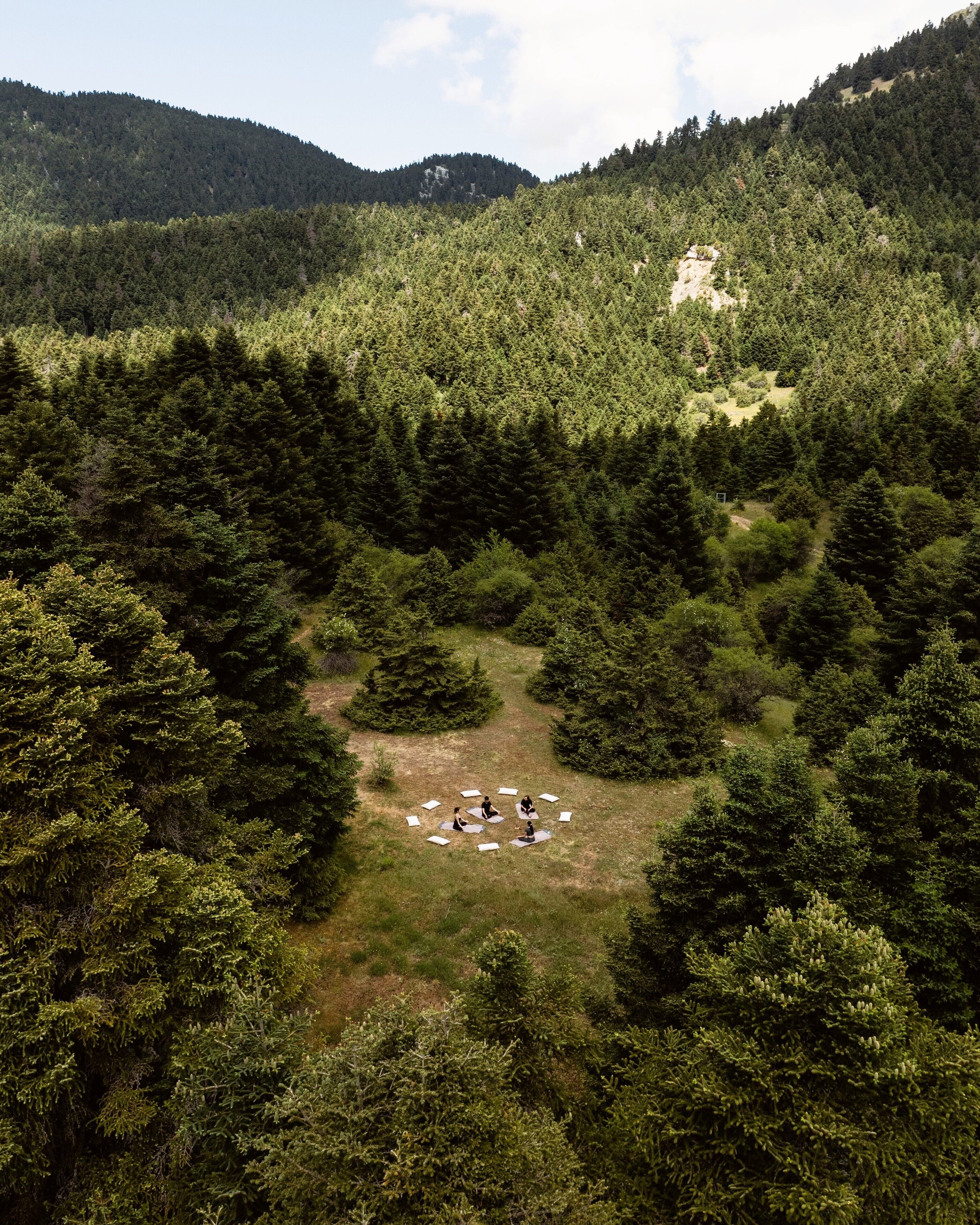 A circular arrangement of tents in a forested area with dense trees and hills in the background.