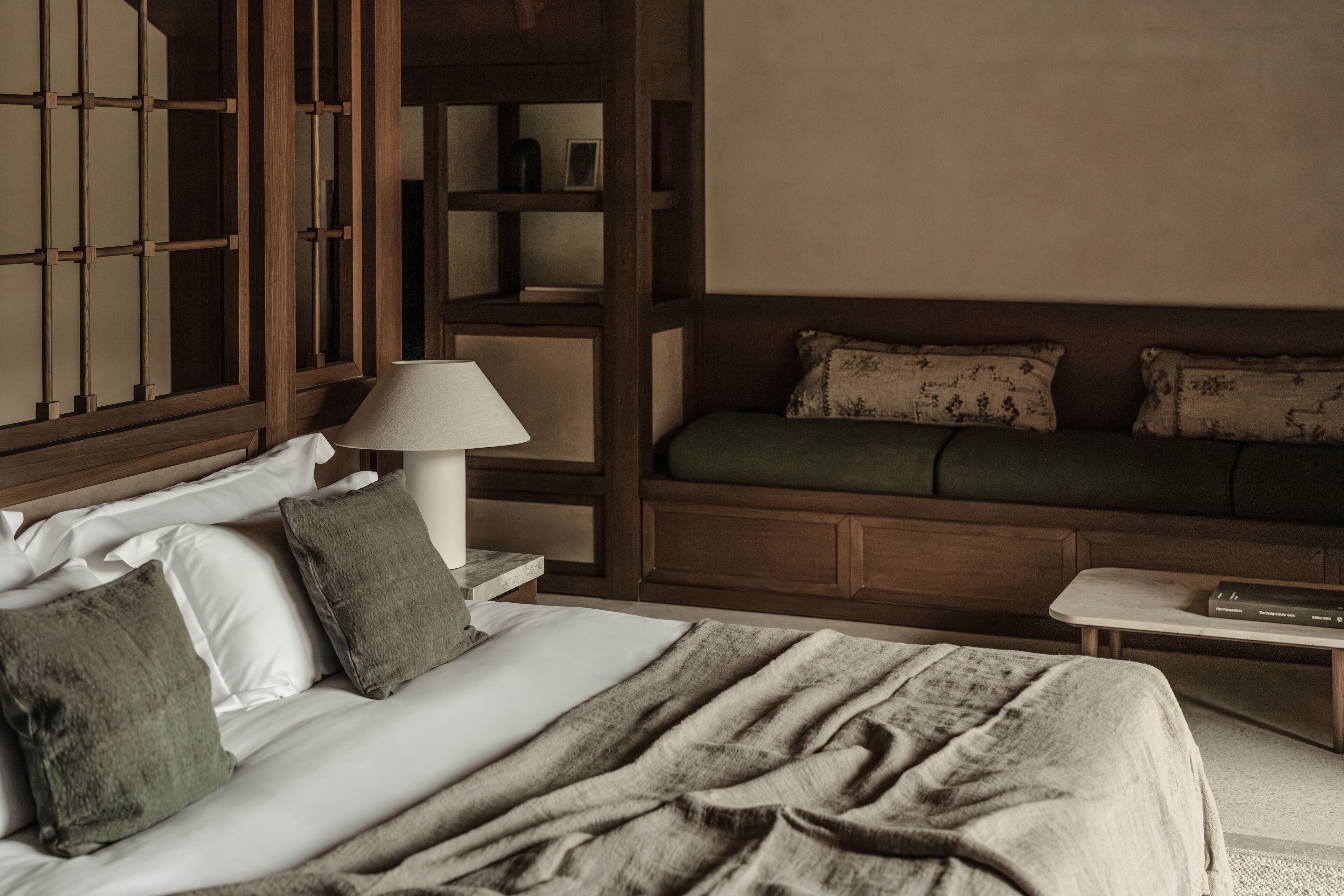 Una habitación de hotel con cama, una mesita de noche con lámpara, un sofá y una estantería de madera.