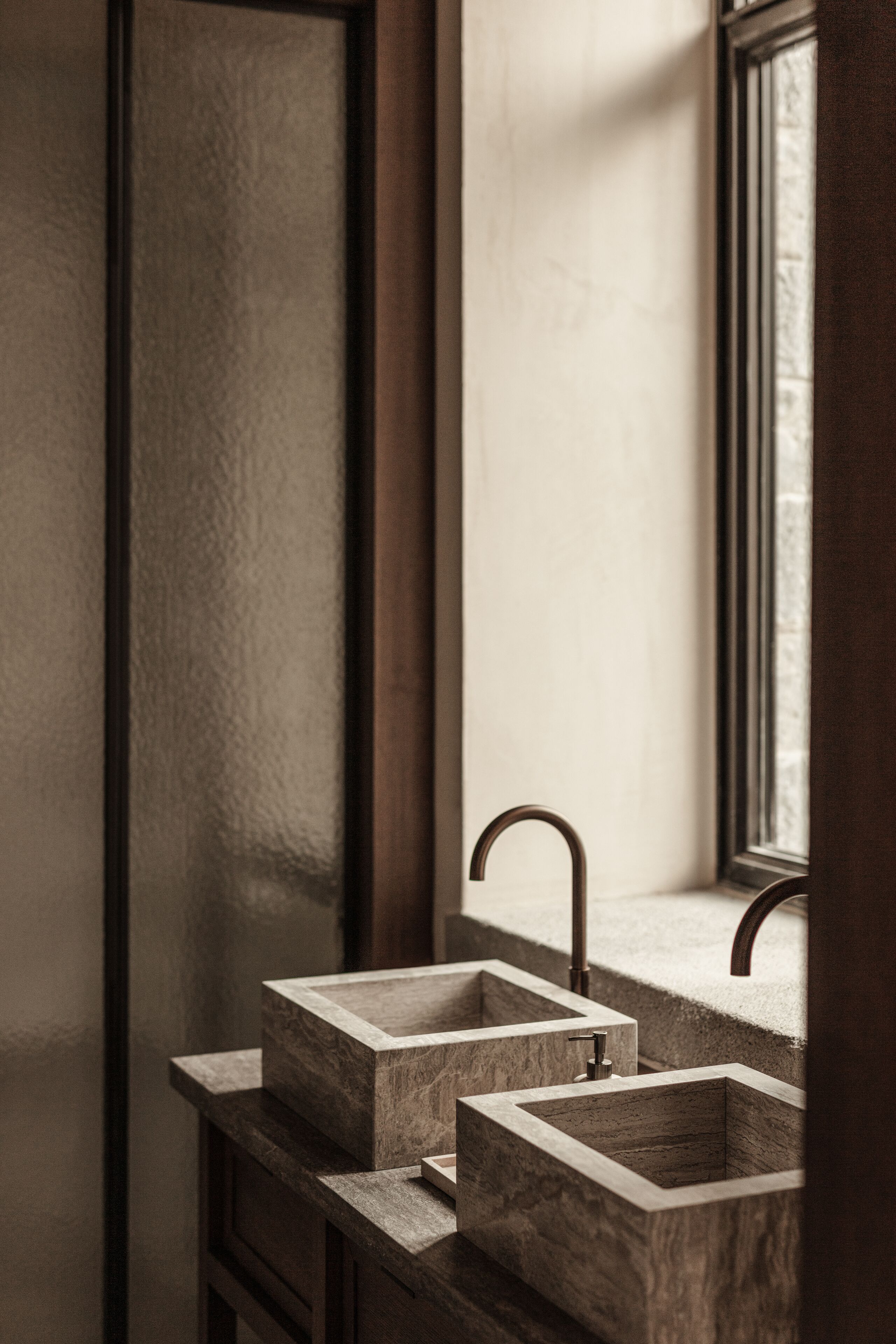 Une salle de bain avec deux vasques rectangulaires faites d’un matériau qui ressemble à de la pierre, une fenêtre avec vue et un meuble en bois.