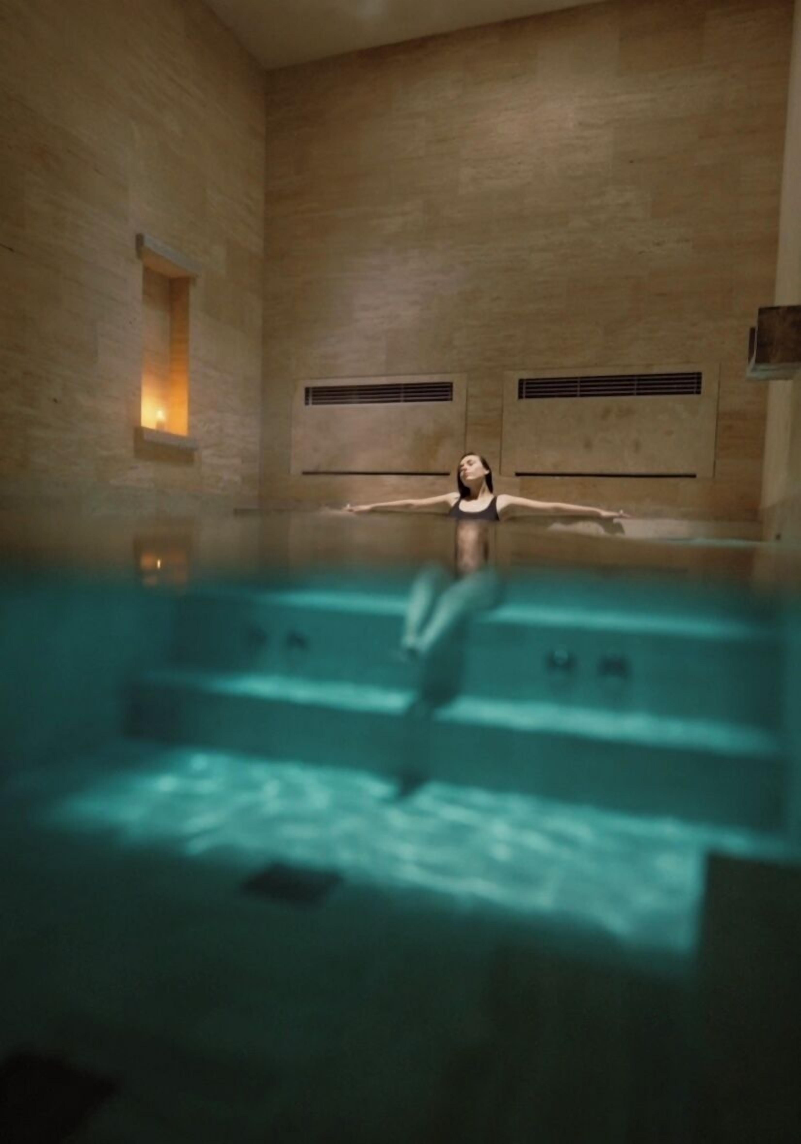 A person in a swimming pool with a stone wall and a small window.