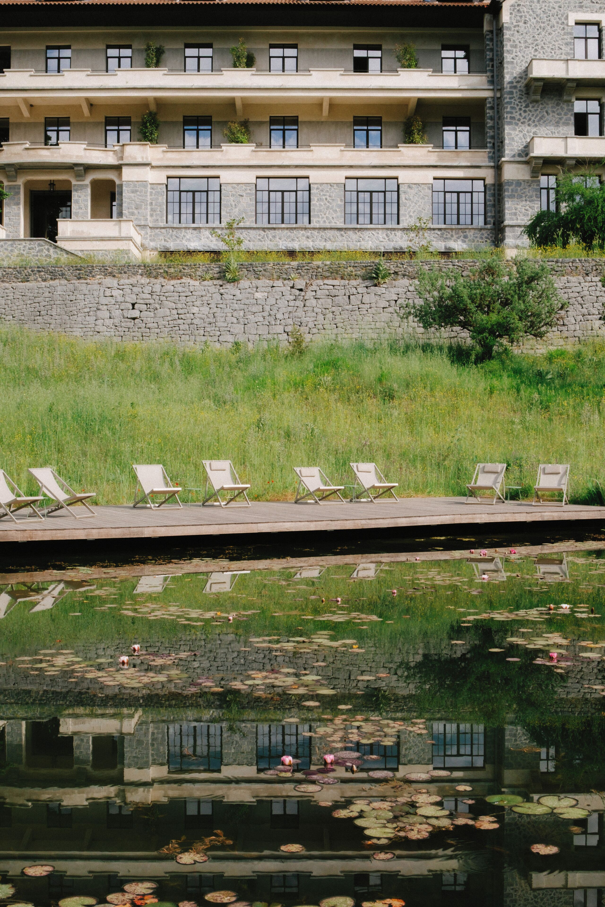 Un edificio con varios balcones, una pared de piedra y una piscina con nenúfares.