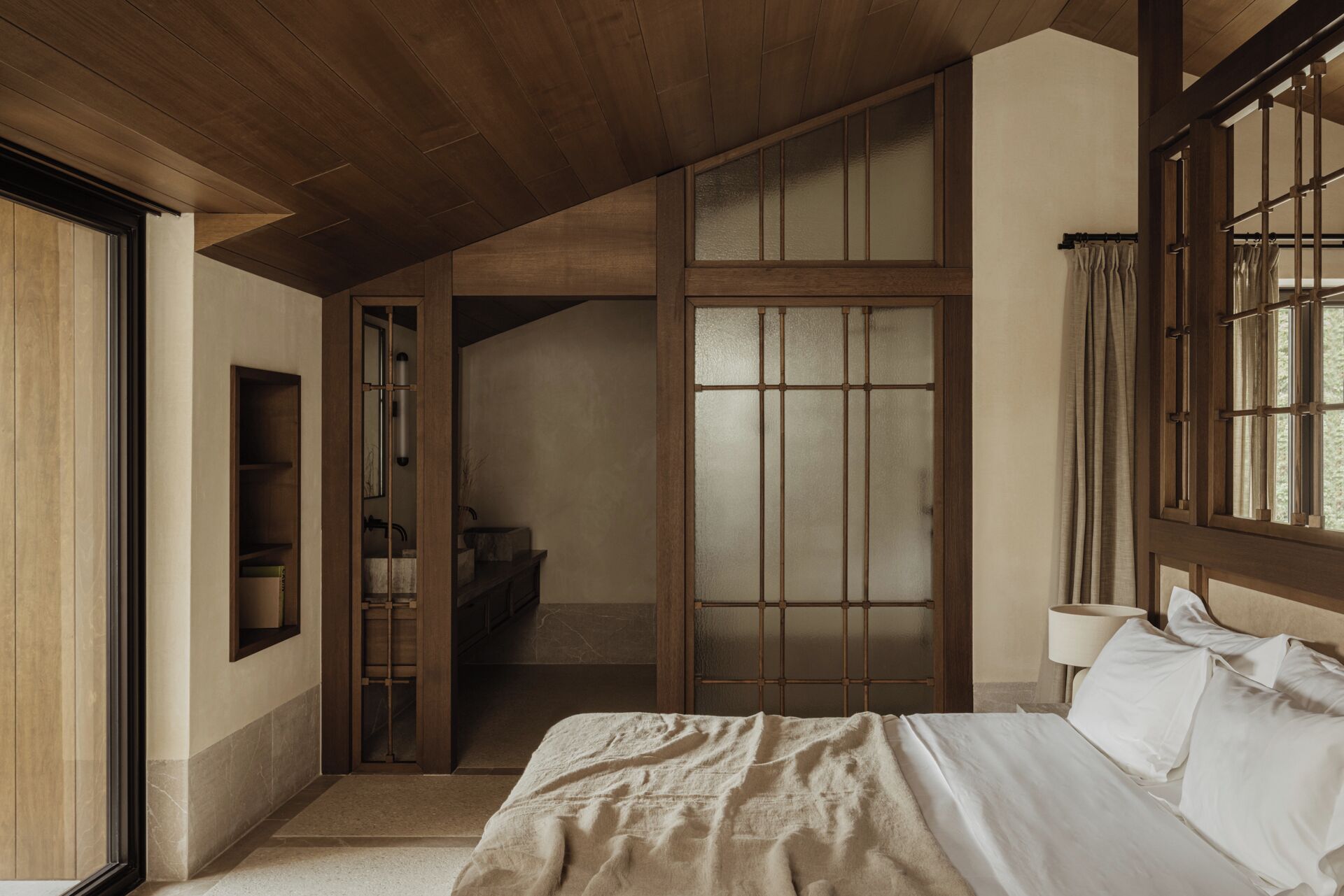 A bedroom with a large bed, a wooden wardrobe, a mirror, and a window with curtains.