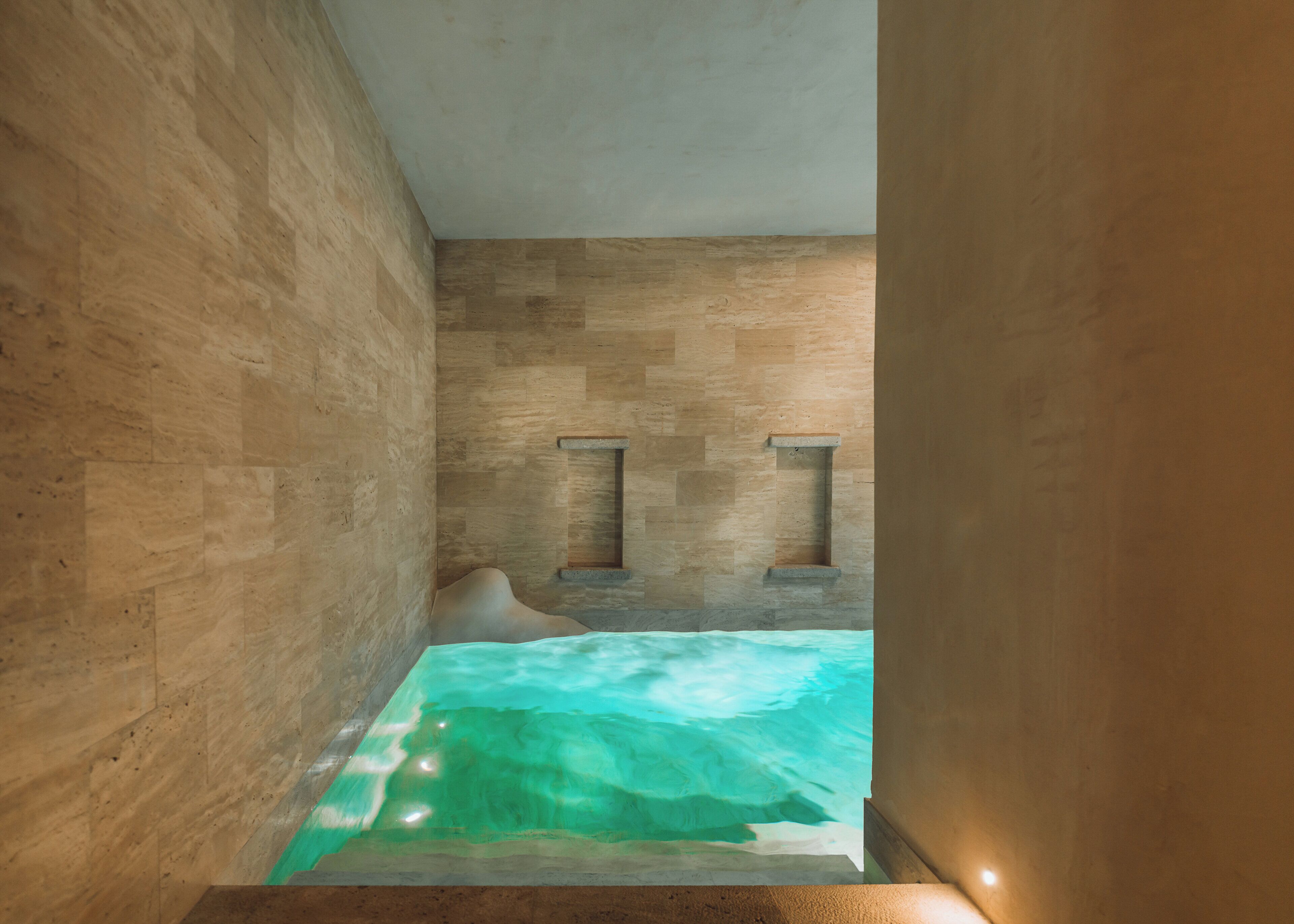 A stone-walled room with a small, rectangular window and a built-in bathtub with clear water.