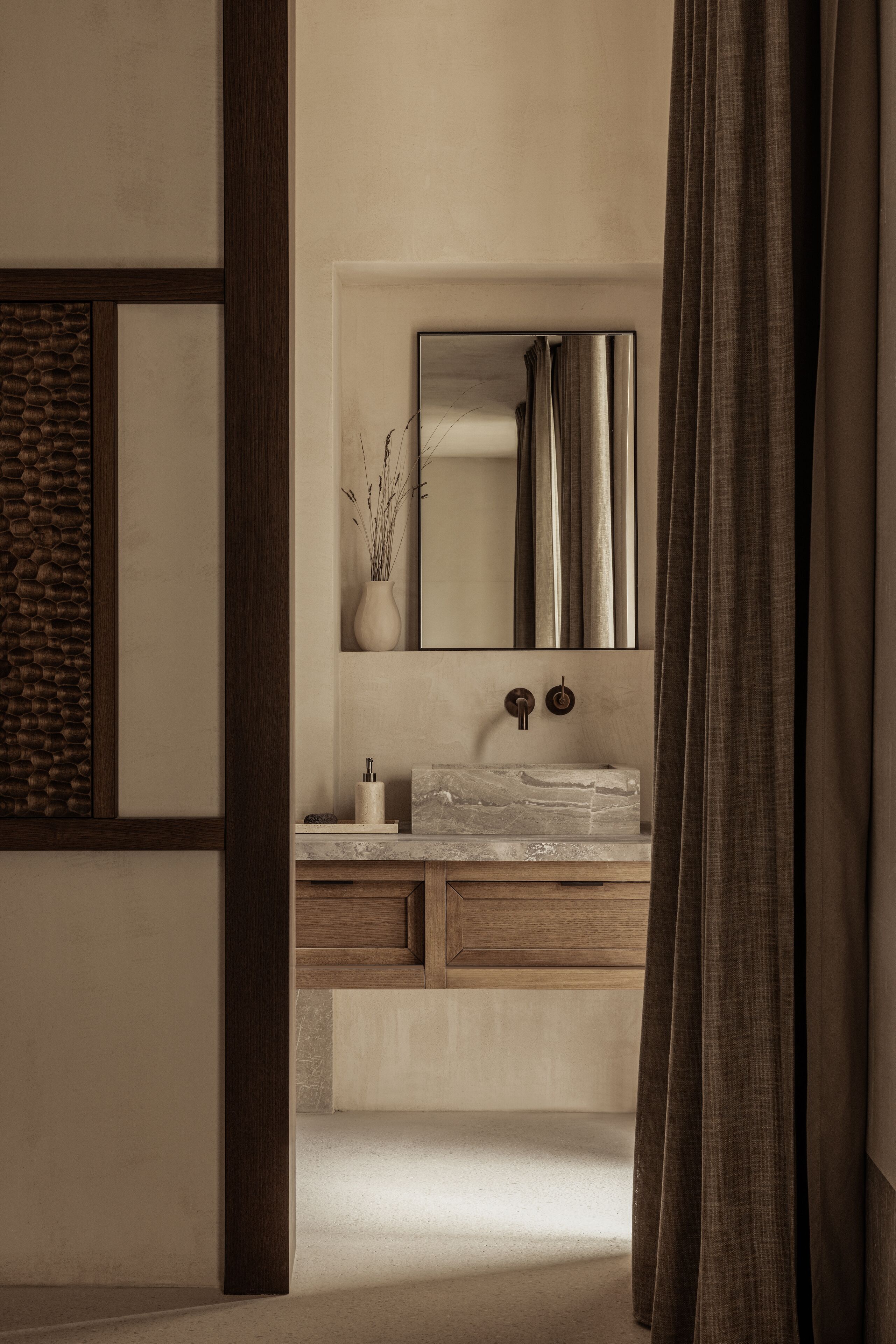 Un baño moderno con lavamanos de mármol, tocador de madera y un espejo grande.