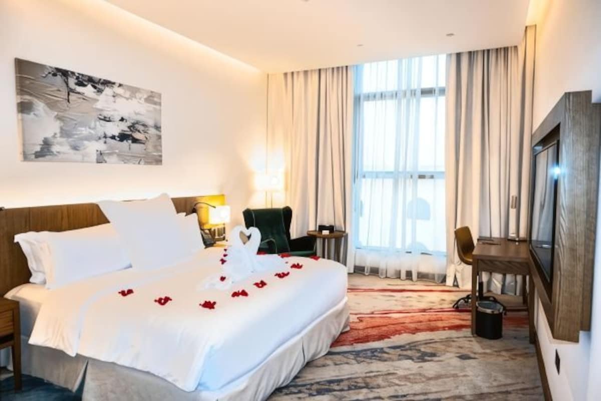 A hotel room with a large bed, a desk, a chair, a TV, and a window with curtains.