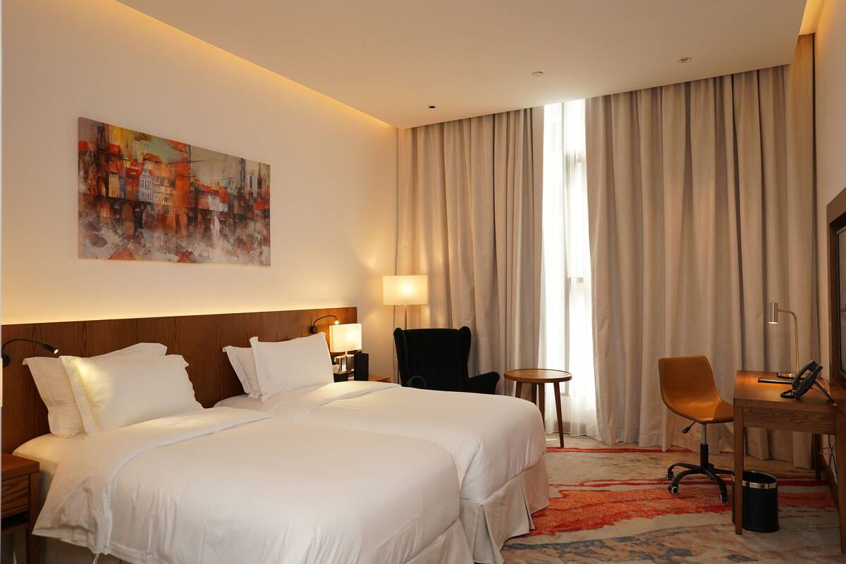 A hotel room with a large bed, a desk with a chair, a television, and a painting on the wall.