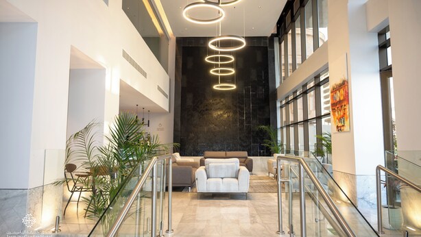 Un moderno vestíbulo de hotel con piso de mármol, un área de descanso central y una escalera con barandales de vidrio.
