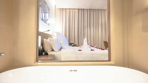 Una habitación de hotel moderna con una cama grande, un baño con bañera y vistas a la ciudad a través de una ventana.